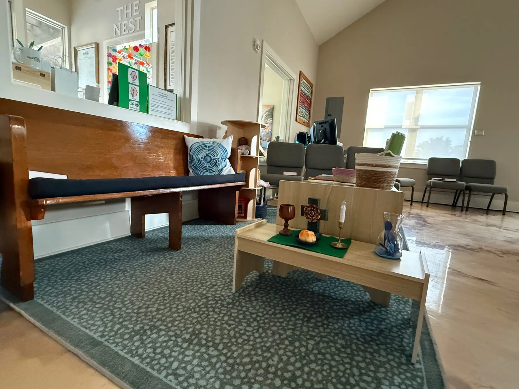 The Pray-Ground at the back of the sanctuary: a wooden pew with cushions, a patterned rug, and a low table set with a cross, a candle and bread.